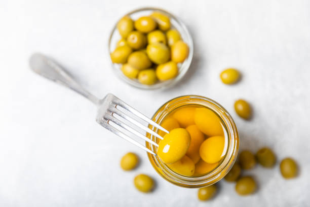 Olives in a glass jar on a white wooden background. pitted green olives in jar.Pickled olives in glass jar. On a wooden background.Marinaded olives. Space for text.Space for copy. Vegan food. aceitunas en un frasco de vidrio sobre un fondo de madera blanca. aceitunas verdes sin hueso en frasco. aceitunas en escabeche en tarro de cristal. sobre un fondo de madera. aceitunas marinadas. espacio para texto. espacio para copiar. comida vegana.