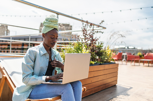 Young adult black woman working outdoors at park using laptop at sunny summer day