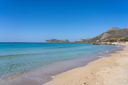 A tranquil scene of blue waters lapping against a beach with majestic mountains in the background at Falasarna beach, Crete Island, Greece
