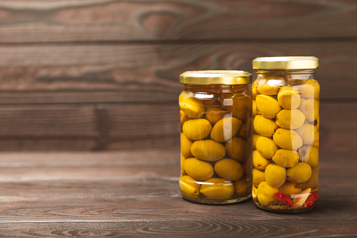 Olives in a glass jar on a brown wooden background. pitted green olives in jar.Pickled olives in glass jar. On a wooden background.Marinaded olives. Space for text.Space for copy. Vegan food.