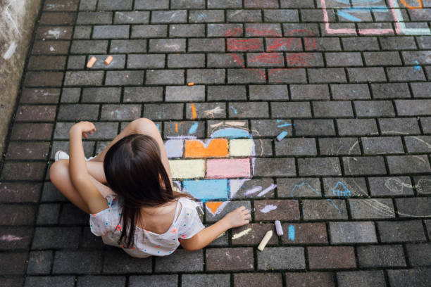 istock Girl sitting on the ground and drawing colorful hearth shape with chalks 1502545090