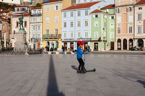 Piran, Slovenia - January 14, 2023: A boy with helmet riding his scooter on a sunny day in Giuseppe Tartini square