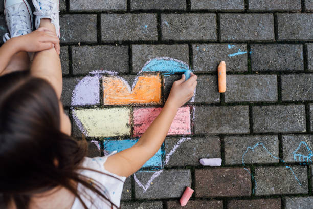 istock Girl sitting on the ground and drawing colorful hearth shape with chalks 1502545197