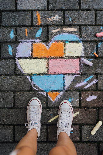 Above shot of Child standing next to a chalk drawing heart shape on the ground .Love and unity concept