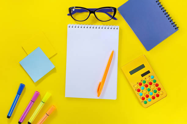 istock Notebook with pen, markers and stickers with calculator and glasses on yellow background. Back to school, business meeting. Copy space 1502545892