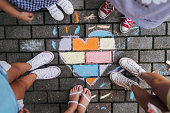 Children standing next to a children’s chalk drawing heart shape on the ground