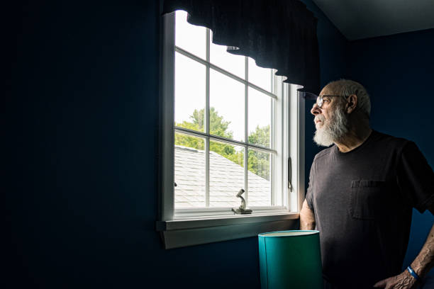 istock Pensive Senior Man Looking Out Window From Dark Room 1502546348