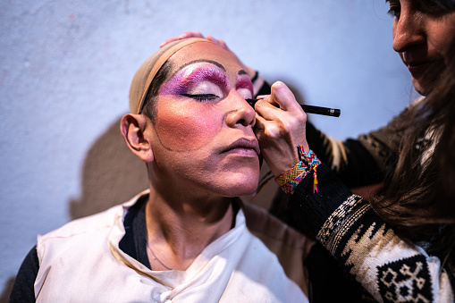 Makeup artist woman doing makeup for drag queen backstage before performance at theater