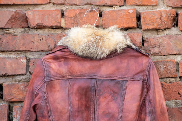 赤い毛皮の革の冬の女性のジャケットは、屋外のレンガの古い壁のハンガーにぶら下がっています、婦人服 - brick red wool heat ストックフォトと画像