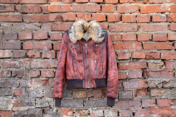 giacca da donna invernale in pelle di pelliccia rossa appesa su un gancio su un vecchio muro di mattoni all'aperto durante , abbigliamento femminile - brick red wool heat foto e immagini stock