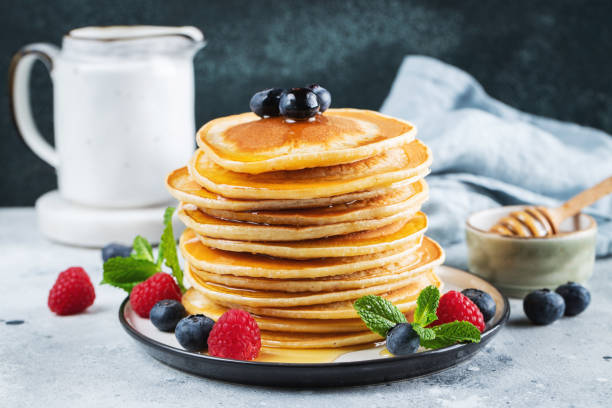 istock Delicious pancakes, with fresh blueberries, raspberry and maple syrup or honey on a dark background 1502558946