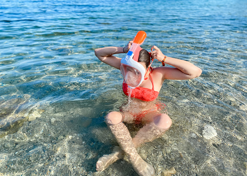 Portrait of young teenage girl in the sea putting on the diving mask