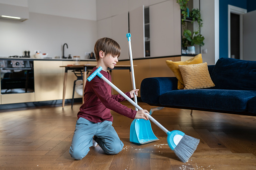 Little boy sweeping floor in living room, kid doing daily regular household chores and helping parents around house, gain important life skills. Children and housework concept