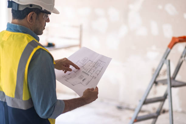 istock Concentrated worker in helmet checking apartment drawing stands in room 1502567443
