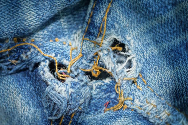 texture from a piece of torn blue white cotton fabric with holes and yellow threads at the seams of old clothes