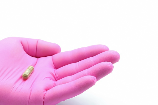 Hand with pink glove showing a Probiotic pill or medication capsule