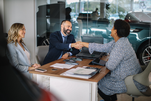 Mid aged couple visits the car dealership, looking at the current offers, talking to the salesperson. They’re sitting at the desk, choosing which colour they like the best, finishing paperwork, getting keys for the new car.