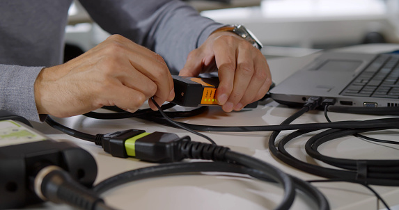 Cropped shot of male it-specialist connect wires to gadget and fix laptop. Close up of hacker or it-technician working with computer using wires and external hard drive