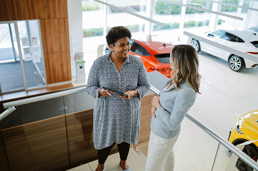 Mid aged woman visits the car dealership, looking at the current offers, talking to the salesperson. Thinking of going EV or staying with the internal combustion car, going through all options.