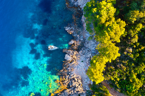 Rocky coast and sail yacht on the sea bay as a background. 
Sea and waves from top view. Blue water background from top view. Top view from drone. Summertime vacation.