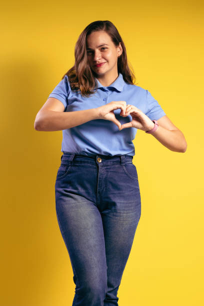 portrait of a brazilian woman, wearing a polo shirt and jeans, making a heart shape with her hands, at the height of her left breast, looking at the camera - belém - pará - brazil - human heart flash imagens e fotografias de stock