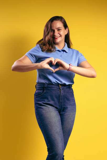 portrait of a brazilian woman, wearing a polo shirt and jeans, making a heart shape with her hands, on her right chest, smiling and looking at the camera - belém - pará - brazil - human heart flash imagens e fotografias de stock