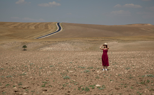 A woman in a red dress and a hat in the middle of the steppe