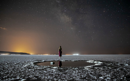 A woman watches the sky in a salt lake under a night view of the Milky Way