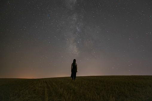 A woman watches the sky in a field under a night view of the Milky Way