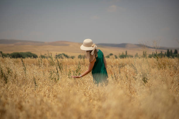 Young woman walking a footpath across a green wheat field. Picturesque summer scene, peaceful rural view, freedom concept