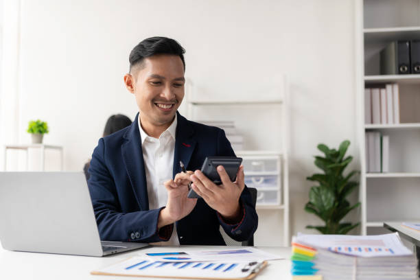 istock Asian businessman writing financial graph chart marketing information plan Male hand using laptop at desk reading financial document spreadsheet for calculation and analysis. 1502629360