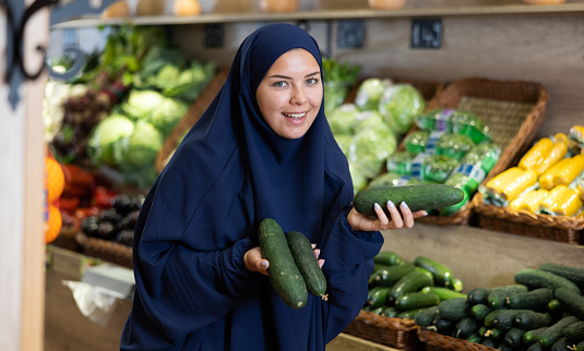 Woman in a veil buys ripe cucumbers in a supermarket
