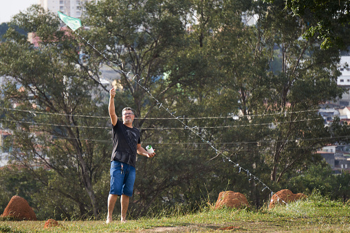 Man flying a kite in a neighborhood public park. The photo was taken from a long distance in the city of Sorocaba in the State of São Paulo.