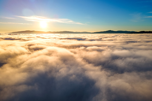 Aerial view of yellow sunset over white puffy clouds with distant mountains on horizon.