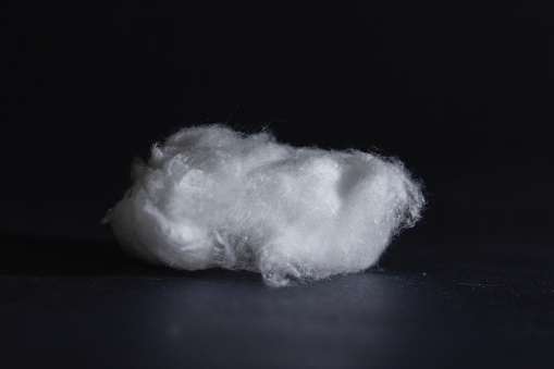 Picture of cotton wool isolated on black background. Cotton wool consists of silky fibers taken from cotton plants in their raw state. Impurities, such as seeds, are removed and the cotton is then bleached using hydrogen peroxide or sodium hypochlorite and sterilized. It is also a refined product which has medical, cosmetic and many other practical uses.