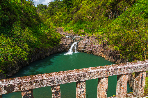 Waterfall running down rocks into a natural swimming hole viewed from a bridge on the road to Hana, Maui, Hawaii.