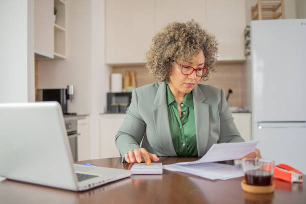 istock Mature woman using calculator while going through bills and home finances 1502654243