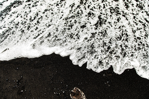 High contrast image of white wave washing over black sand beach in Honokalani, Maui, Hawaii.