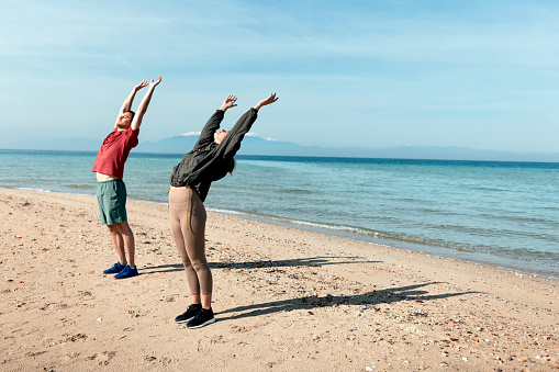 Man and woman doing yoga flow on the sunny beach
