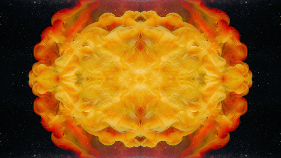 Fluid kaleidoscope. Paint water. Ink drop. Yellow red orange color smoke cloud explosion symmetrical pattern on dark black glitter texture abstract background.