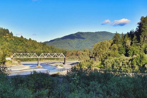 A rural California landscape with a railway truss bridge in Humboldt Redwoods State Park is the location of the once-thriving community of Dyerville, whose demise occurred through two major floods of the Eel River in the early and mid-20th century.