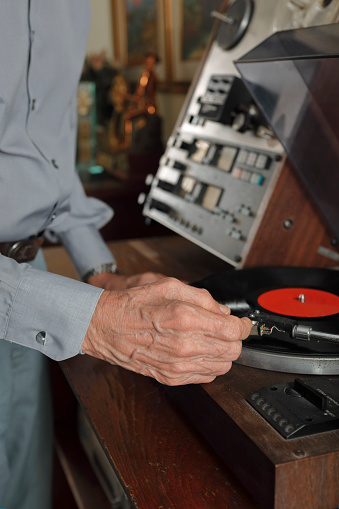 Elderly man's hand placing the needle on a vintage vinyl record player.