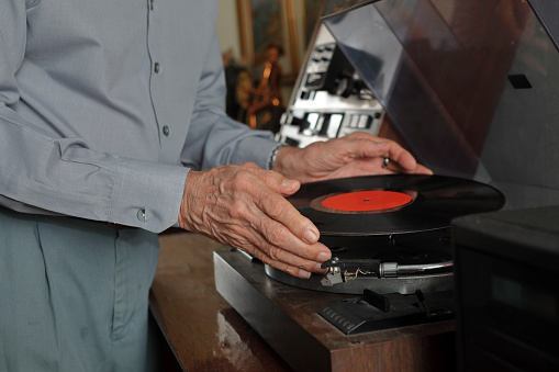 Elderly man's hand placing a vinyl in disc player.