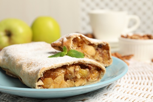 Delicious strudel with apples, nuts and raisins on wicker mat, closeup