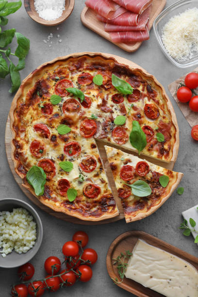istock Cut delicious homemade quiche with prosciutto and ingredients on light grey table, flat lay 1502697770