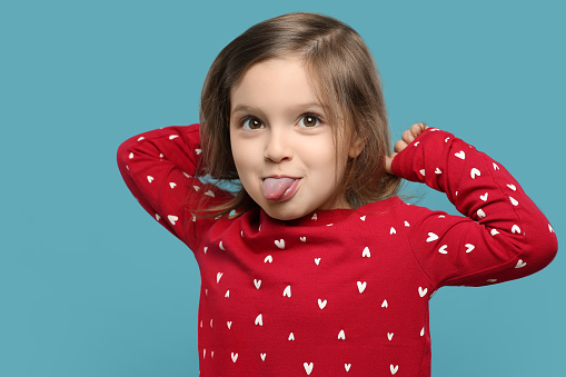 Funny little girl showing her tongue on light blue background
