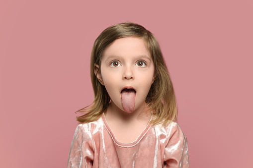 Funny little girl showing her tongue on pink background