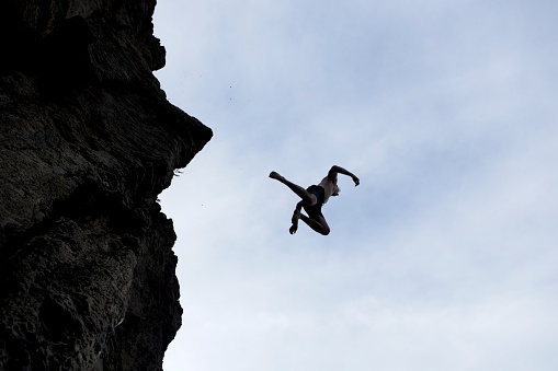 A silhouette of a young man jumping off a high rock into the water below in southern Idaho.
