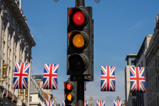 The stoplight, traffic light with both amber and red lights lit can also be used in a conceptual design, a metaphor for life choices, hard decisions and choosing the right path, direction in life. External signs to point you in the right direction. semáforo, un semáforo amarillo y rojo en una calle de la ciudad de londres, inglaterra. banderas rojas, blancas y azules de union jack, banderas del reino unido en el fondo. señales confusas, señales mixtas, así que tenga cuidado al conducir o tome un