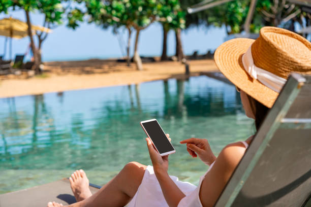 Young woman traveler relaxing and using a mobile phone by a resort pool while traveling for summer vacation, Travel lifestyle concept stock photo